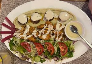 Ce plateau méditerranéen se compose de falafels servis sur un lit de houmous, nappés d’une sauce crémeuse à base de tahini
