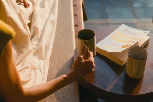 Une main de femme posant un café du matin sur une table de chevet avec un livre et un verre d'eau.